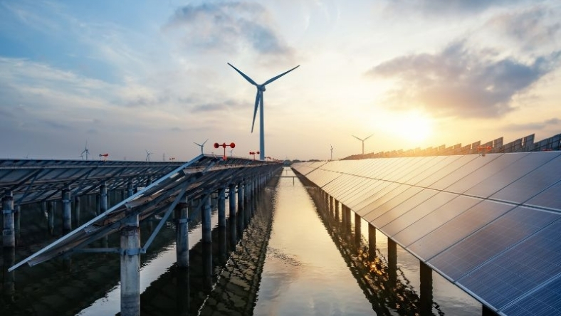 Utility-scale solar panels and wind turbine at sunset