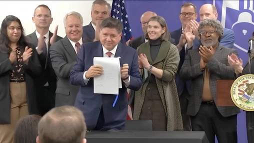 Man holds a signed document while officials applaud during a government signing ceremony