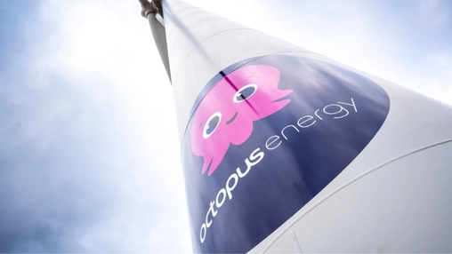 Upward angle view of a wind turbine displaying the Octopus Energy logo and pink octopus mascot on the nacelle